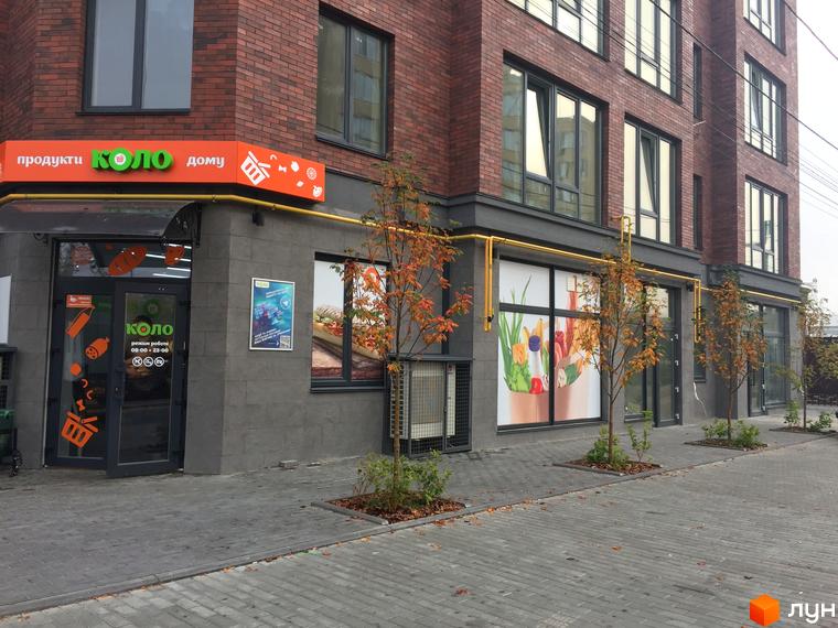 Фасад житлового будинку Brick House з магазином на першому поверсі. Тротуари викладені плиткою, вздовж будівлі висаджені дерева.