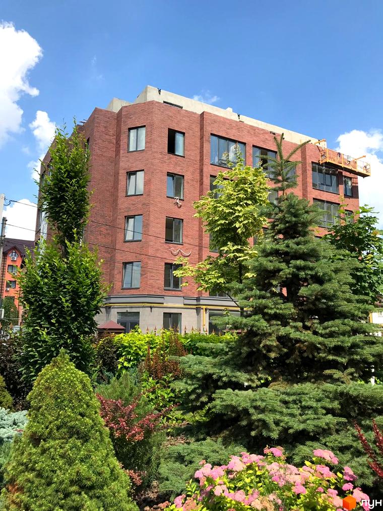 Клубний будинок Brick House – цегляна будівля з темними вікнами, оточена доглянутим зеленим ландшафтом з різноманітними деревами та квітучими кущами.