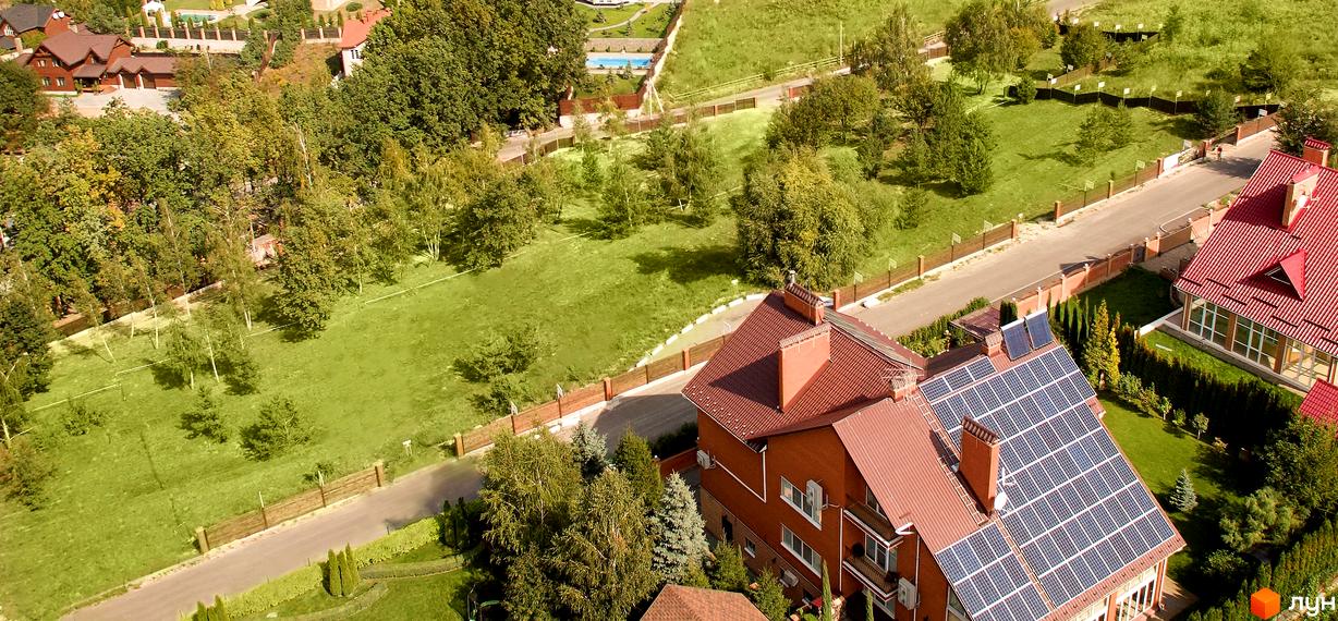 Котеджне містечко KM Lisnyky Club з будинками з червоними дахами та сонячними панелями. На території комплексу є зелені газони, дерева та доріжки.