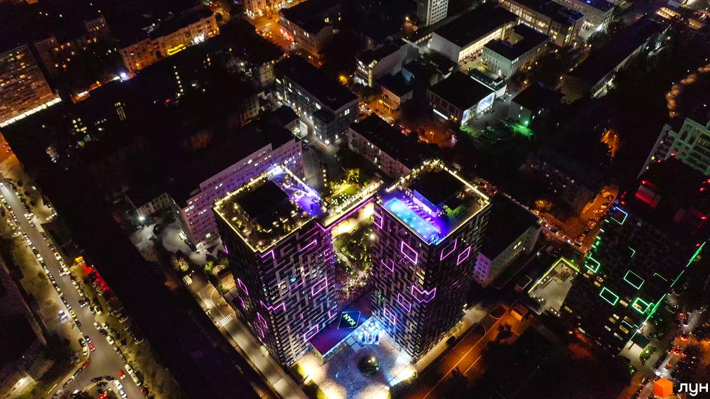 Житловий комплекс Tetris Hall вночі з підсвіченими фасадами та басейном на даху. Сучасна архітектура та освітлення створюють унікальний вигляд будівлі.