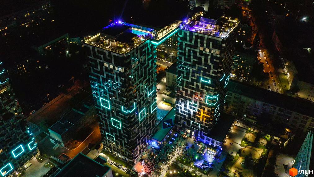 Житловий комплекс Tetris Hall вночі з яскравою підсвіткою фасадів та зоною відпочинку на даху. Територія навколо комплексу облаштована зонами для дозвілля.
