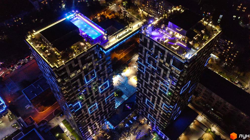 Житловий комплекс Tetris Hall з басейном та зоною відпочинку на даху, підсвічений неоновими вогнями. Сучасна архітектура та освітлення фасаду створюють вражаючий вигляд.