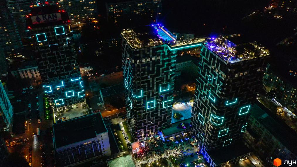 Житловий комплекс Tetris Hall у Києві вночі. Будинки з геометричним візерунком та неоновим підсвічуванням. На даху одного з будинків басейн та зона відпочинку.