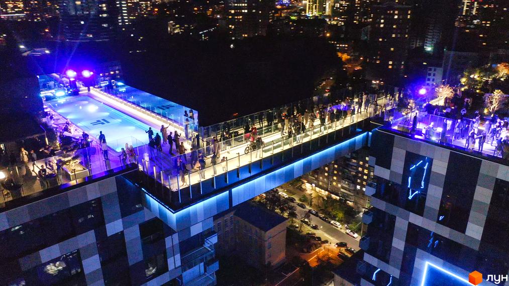 Житловий комплекс Tetris Hall з басейном та зоною відпочинку на даху в нічний час. Сучасна архітектура та освітлення комплексу.