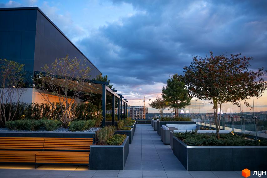 Тераса житлового комплексу Tetris Hall з лаунж зоною та міським пейзажем на заході сонця. Сучасна архітектура та зелені насадження створюють затишну атмосферу.