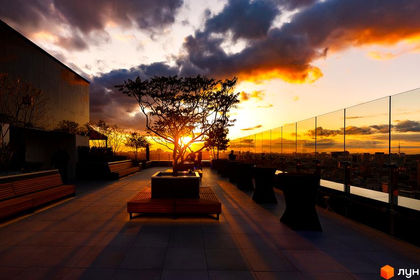 Житловий комплекс Tetris Hall на фоні заходу сонця з видом на місто. Тераса з лаунж-зоною та деревами.