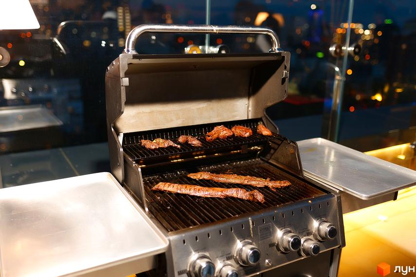 Житловий комплекс Tetris Hall: м'ясо готується на грилі на відкритій терасі з панорамним видом на місто ввечері.