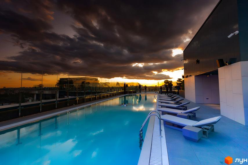 Басейн на даху ЖК Tetris Hall з шезлонгами та видом на місто на заході сонця. Сучасна архітектура комплексу та навколишня територія.