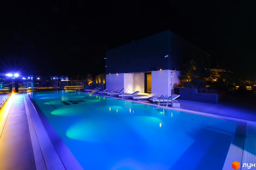 Нічний вигляд басейну на даху житлового комплексу Tetris Hall з шезлонгами та підсвіткою. Територія навколо басейну облаштована для відпочинку.