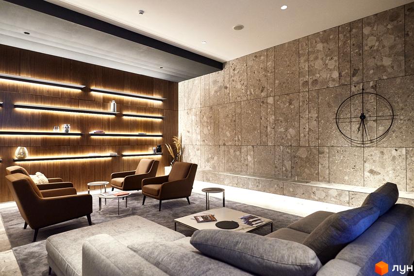 Інтер'єр вітальні в ЖК Tetris Hall з коричневими кріслами та диваном, дерев'яною стіною з підсвічуванням та кам'яною стіною з годинником.