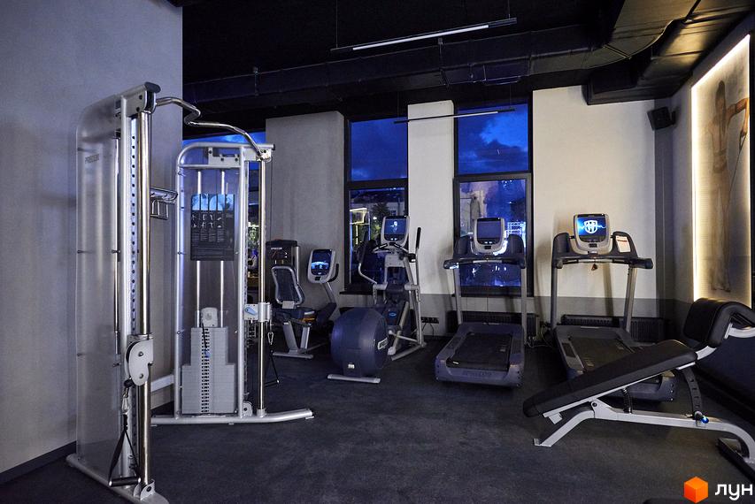 Сучасний фітнес-центр у ЖК Tetris Hall з різноманітними тренажерами: бігові доріжки, еліптичні тренажери, велотренажери та силові тренажери. Простір для тренувань з панорамними вікнами.