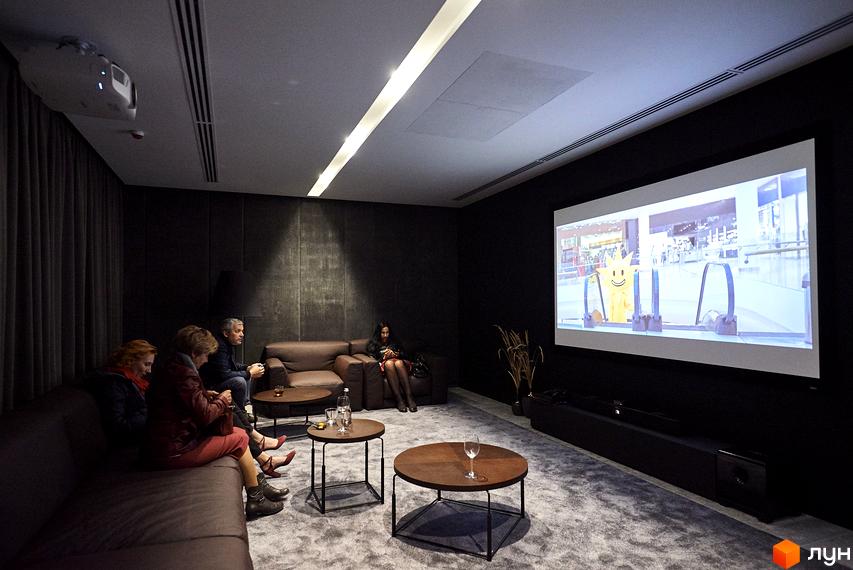 Житловий комплекс Tetris Hall: люди дивляться фільм у кінозалі з великим екраном та зручними диванами. Сучасний дизайн інтер'єру.