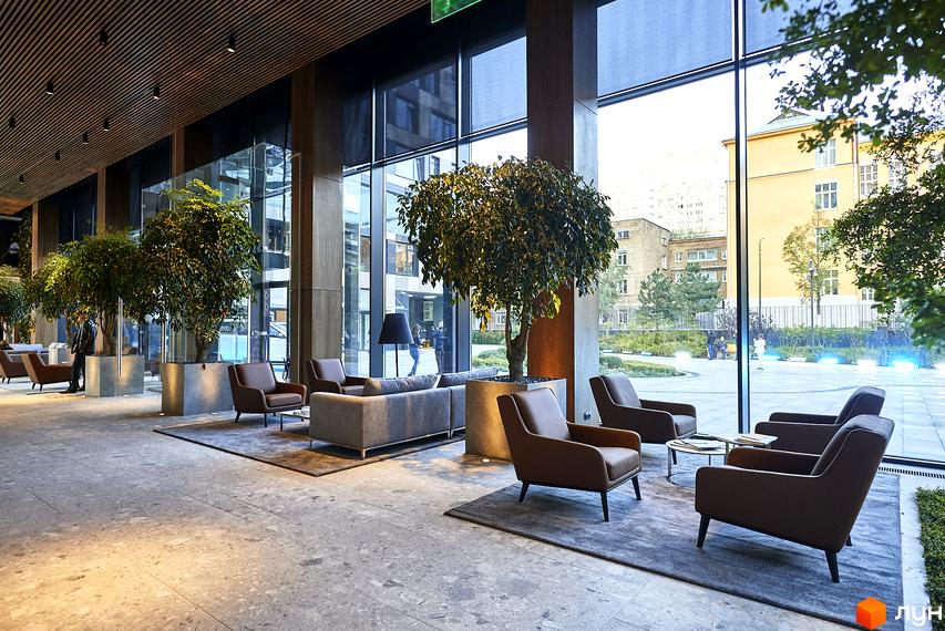 Інтер'єр лобі житлового комплексу Tetris Hall з великими вікнами, дизайнерськими меблями та зеленими рослинами. З вікон відкривається вид на прибудинкову територію з освітленням.