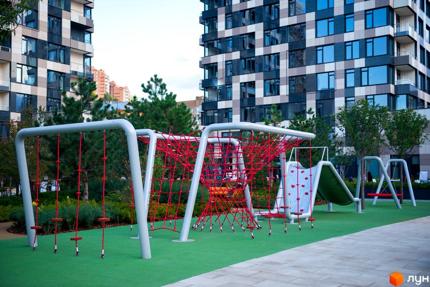 Дитячий майданчик біля житлового комплексу Tetris Hall з червоною сіткою для лазіння та гіркою. На задньому плані видно сучасну будівлю з візерунком з квадратів.