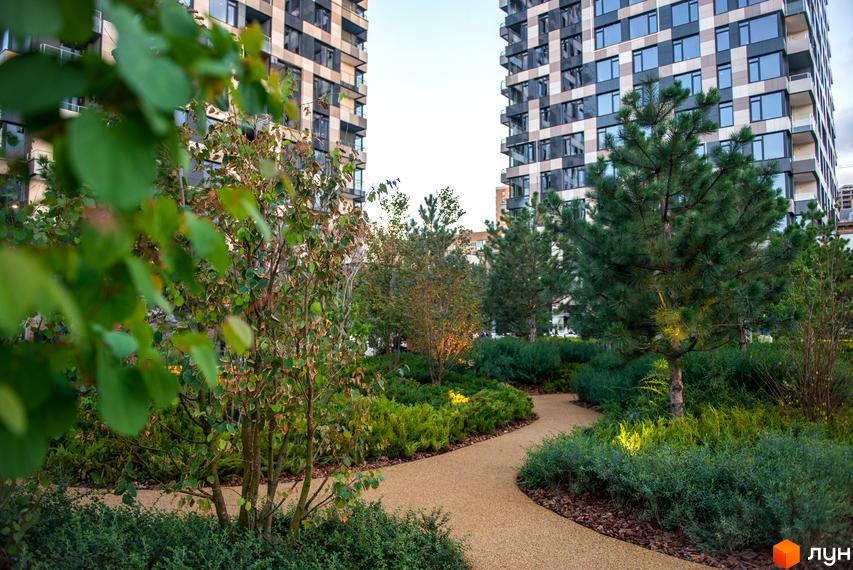 Житловий комплекс Tetris Hall з багатою прибудинковою територією, що включає зелені насадження та пішохідні доріжки.