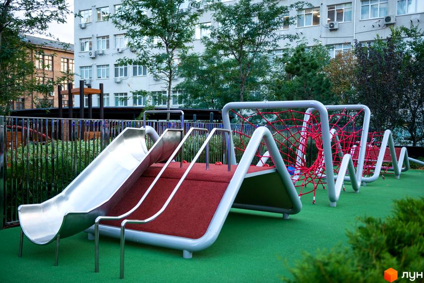 Дитячий майданчик з гірками та сіткою для лазіння на території житлового комплексу Tetris Hall. Сучасна архітектура будинків на фоні.