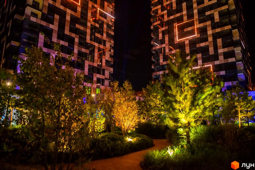 Житловий комплекс Tetris Hall вночі з підсвіченими фасадами та ландшафтним дизайном прибудинкової території. Сучасна архітектура та освітлення створюють унікальну атмосферу.