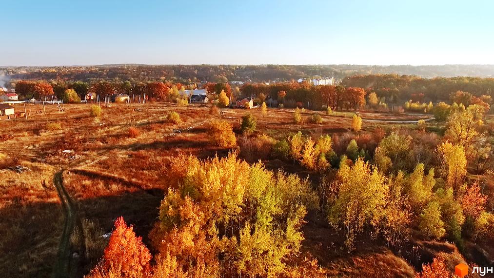 Котеджне містечко Панорама у осінньому пейзажі з жовто-червоними деревами та травою. Навколо видно невеликі будинки та зелені насадження.