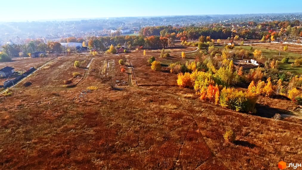 КМ Панорама - це житловий комплекс, що розташований на пагорбі серед осінніх дерев. На зображенні видно частину житлового комплексу та прибудинкову територію з зеленими насадженнями.