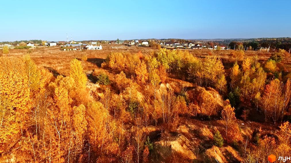 Панорамний вид на житловий комплекс КМ Панорама з осінніми деревами та мальовничим ландшафтом. Навколо комплексу розташовані зелені насадження та невисокі будівлі.