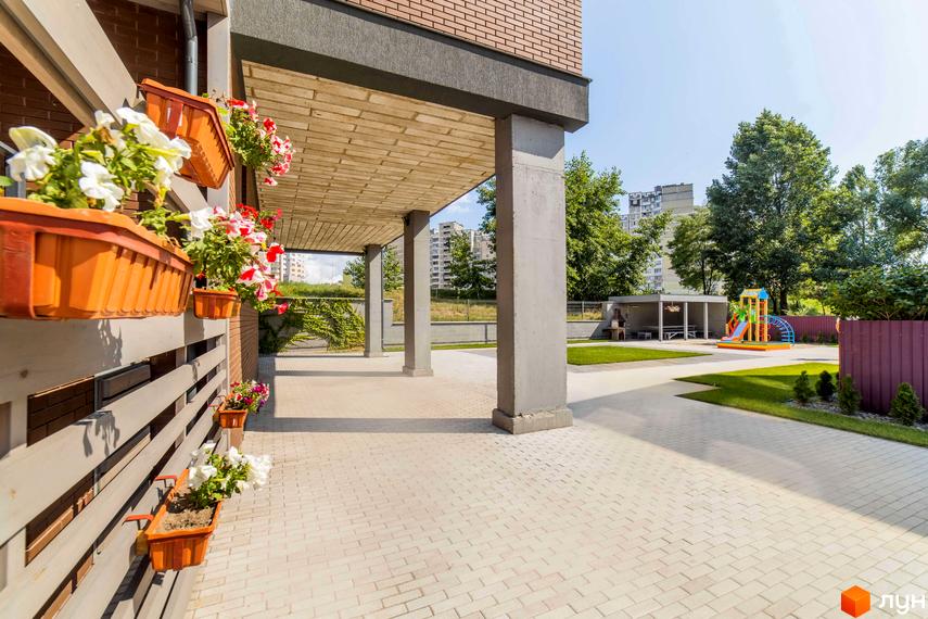 Клубний будинок „Деснянський DeLuxe“ з квітами на фасаді та дитячим майданчиком на прибудинковій території. Огляд території житлового комплексу.