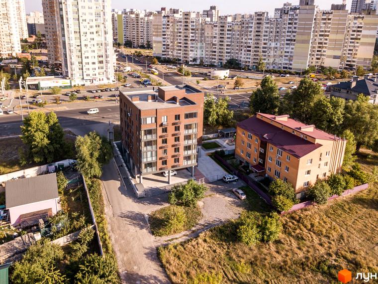 Клубний будинок „Деснянський DeLuxe“ з цегляним фасадом та великими вікнами. Навколо новобудови розташовані дерева та інші будинки.