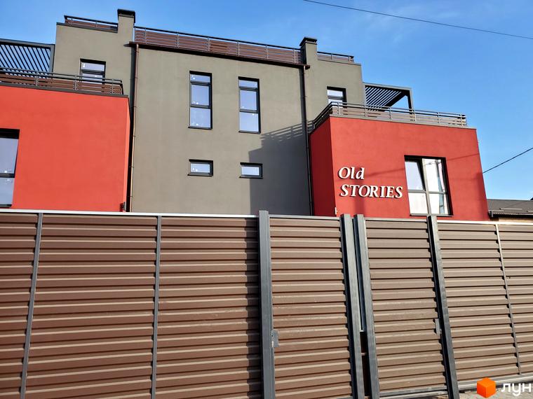 Таунхауси Old Stories: фасади будівель з червоними та сірими елементами, вікна, балкони та коричневий паркан на тлі блакитного неба.