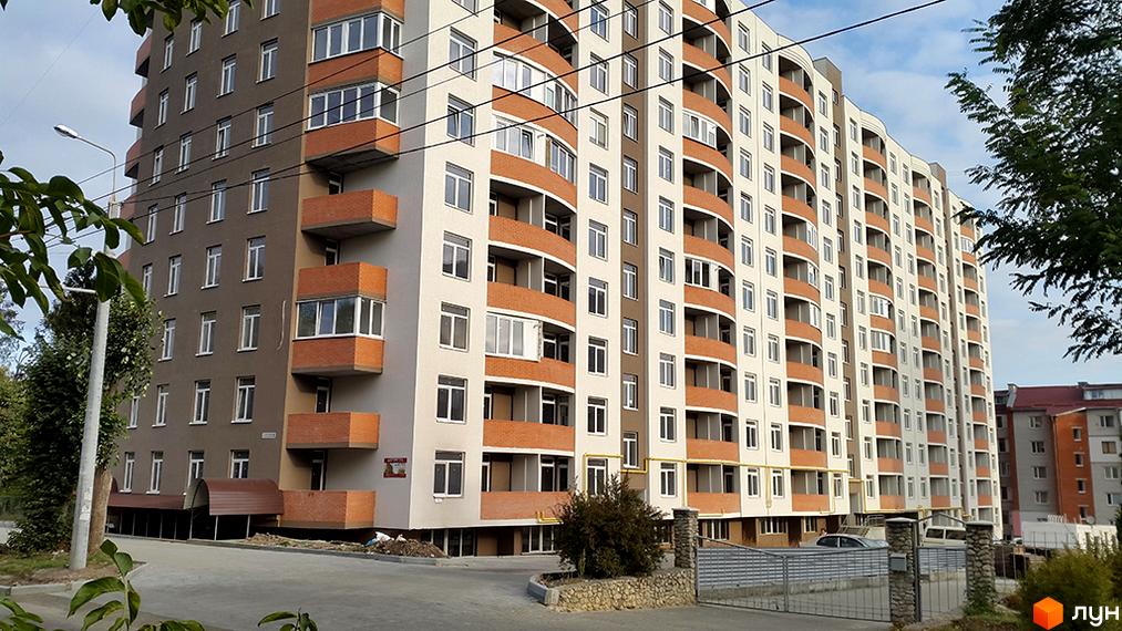 Новобудова на вулиці Сахарова. Багатоквартирний будинок з балконами та сучасними вікнами. Прибудинкова територія з дорогою та парканом.