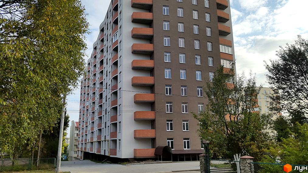 Новобудова на вулиці Сахарова. Багатоповерховий будинок з балконами та вікнами, поруч дерева та паркан.