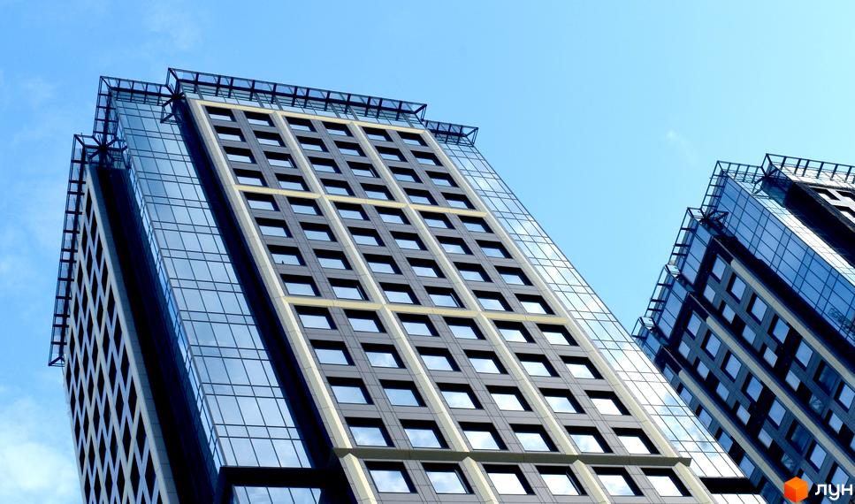 Сучасний житловий комплекс Metropole із скляними фасадами та великою кількістю вікон, що відбивають небо. Будівля має чіткі геометричні форми та виглядає вражаюче на тлі блакитного неба.