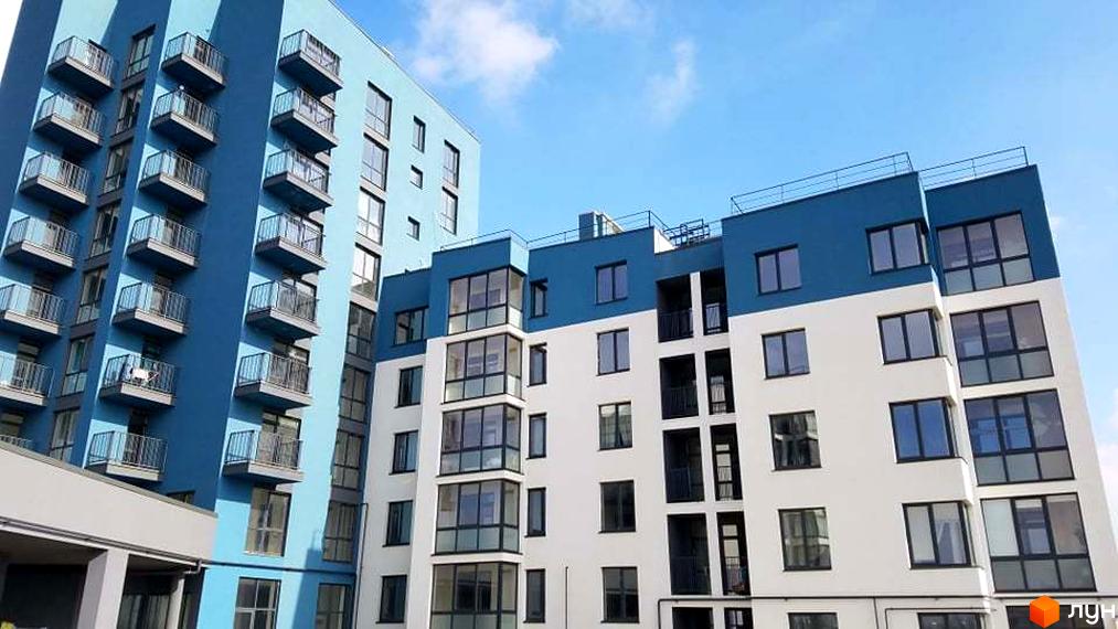 Житловий комплекс Басів схил. Високі будинки блакитного та білого кольорів з численними балконами та великими вікнами на тлі ясного неба.