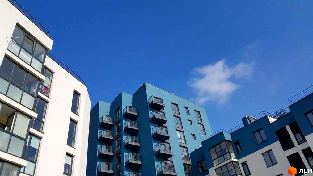 Новобудова ЖК Басів схил з білими та блакитними фасадами, балконами та великими вікнами на тлі ясного неба. Зовнішній вигляд будинку.