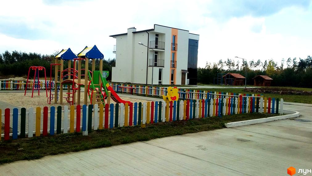 Фото Житлового комплексу Ясний з дитячим майданчиком та кольоровим парканом. Вигляд новобудови з прибудинковою територією.