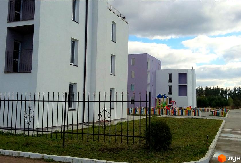 Зображення фасаду та прибудинкової території Житлового комплексу Ясний. Вигляд новобудови з дитячим майданчиком та огорожею.