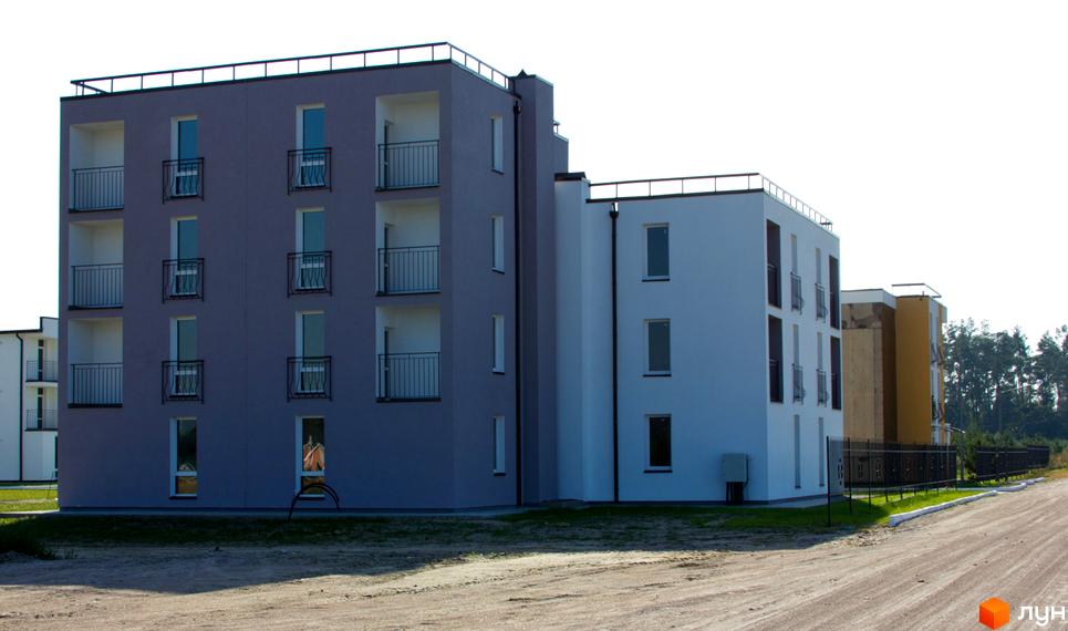 Зображення житлового комплексу Ясний. Багатоповерховий будинок з балконами та великими вікнами, поруч піщана дорога.