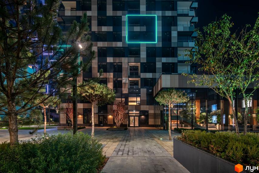 Житловий комплекс Tetris Hall з фасадом, оздобленим геометричними елементами, та підсвіченим квадратом. Навколо комплексу облаштована прибудинкова територія з деревами та освітленням.