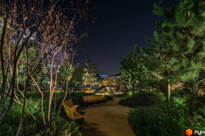 Житловий комплекс Tetris Hall: нічний вид на сучасний дитячий майданчик із лавками та освітленням. Навколо зелені насадження та дерева.