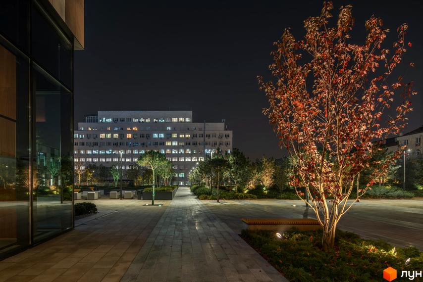 Житловий комплекс Tetris Hall вночі. Зовнішній вигляд будівлі з численними вікнами, освітленими зсередини. Прибудинкова територія з деревами та лавками.