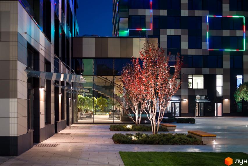Житловий комплекс Tetris Hall вночі. Сучасна архітектура будівлі з підсвічуванням та доглянута прибудинкова територія з деревами та лавками.