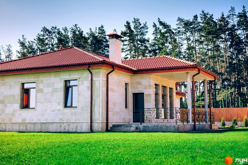 Котеджне містечко КМ Villa Grace - одноповерховий будинок з червоною черепичною покрівлею та світлим фасадом, розташований на доглянутій зеленій ділянці з деревами.