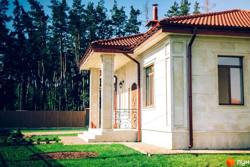 Зовнішній вигляд будинку KM Villa Grace з черепичним дахом та світлими стінами, на тлі соснового лісу та зеленої галявини.