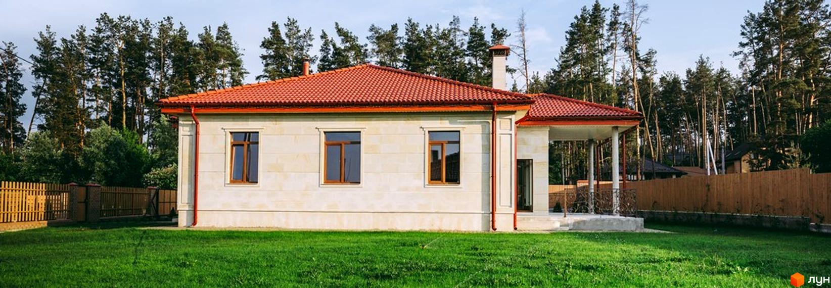 Котеджне містечко КМ Villa Grace: одноповерховий будинок з червоною черепичною покрівлею та великими вікнами на тлі лісу. Доглянута галявина та дерев'яний паркан перед будинком.