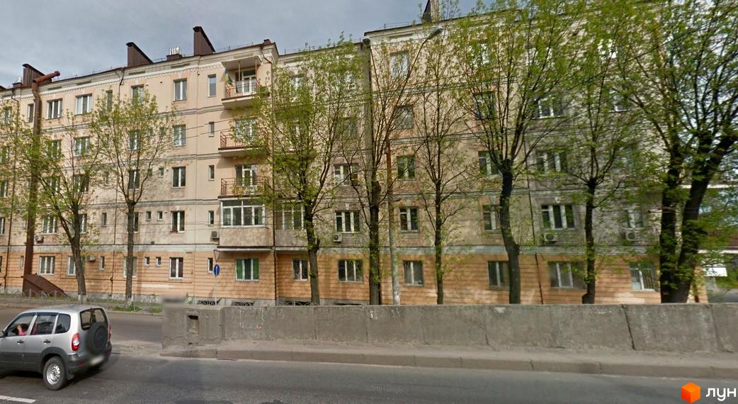 Зовнішній вигляд житлового комплексу на вулиці Довженка, 2. Будинок має світло-бежевий фасад, балкони та дерева перед ним.