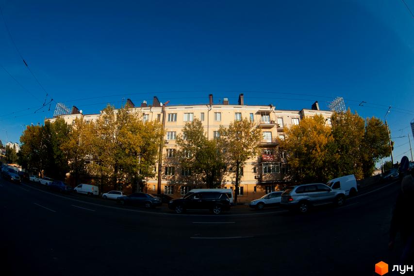 Зовнішній вигляд житлового комплексу на вул. Довженка, 2. Будинок з жовтим фасадом та деревами з жовтим листям поруч.