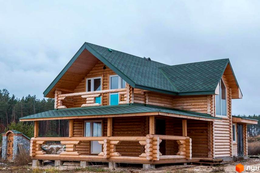 Двоповерховий дерев'яний будинок з зеленим дахом та великою терасою. Котеджне містечко Святобор оточене лісом.