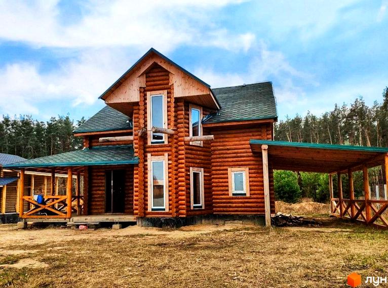 Котеджне містечко Святобор: двоповерховий дерев'яний будинок з навісом та верандою на тлі лісу.