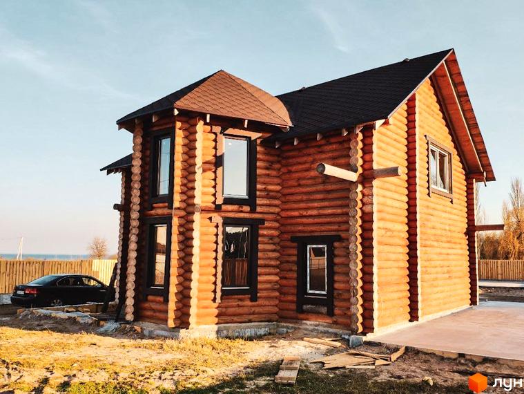 Котеджне містечко Святобор: двоповерховий дерев'яний будинок з темним дахом та вікнами, поруч припаркований чорний автомобіль.