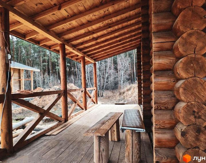 Котеджне містечко Святобор: дерев'яний будинок з терасою та лавками на тлі лісу. Прибудинкова територія з лісовими деревами та будівництвом.