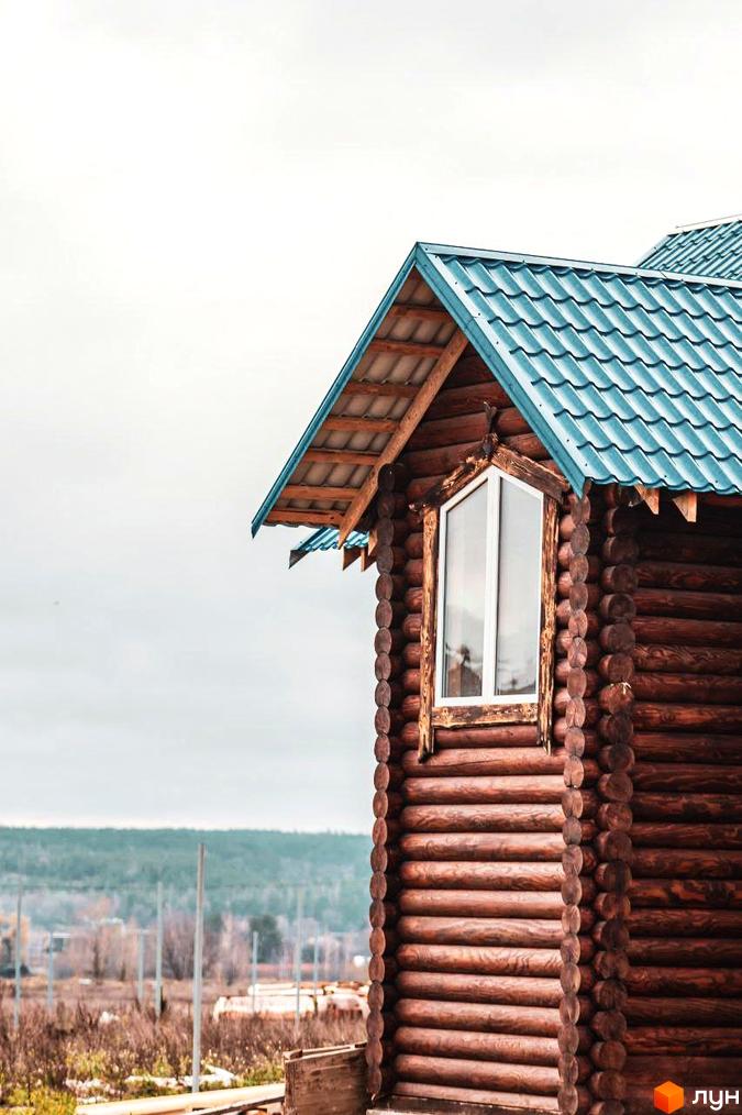 Котеджне містечко КМ Святобор: дерев'яний будинок з блакитним дахом на фоні лісу та неба.