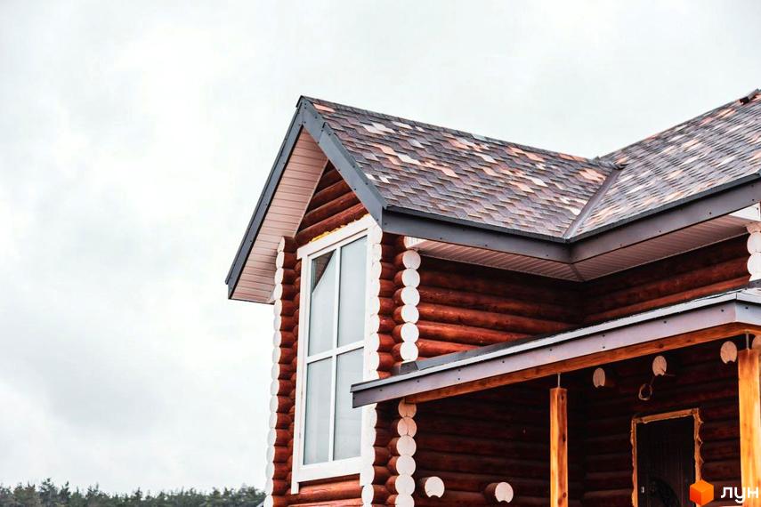 Котеджне містечко КМ Святобор: дерев'яний будинок з вікном та черепичним дахом. Навколо зелені дерева під сірим небом.
